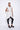 A woman wearing a sleeveless light grey trench-style Vest with a double-breasted button front, notched lapel collar and flap pockets on either side of the waist, asymmetrical hem line, paired with black leggings and chunky black open-toe heels over a white background.