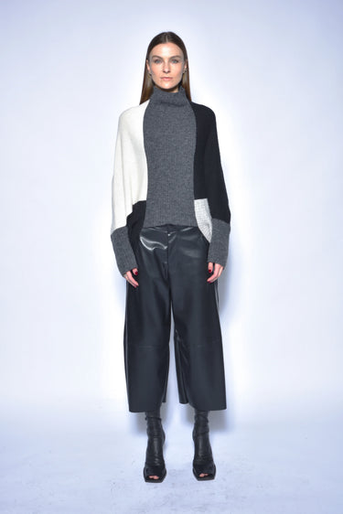 Model wearing a gray turtleneck, black and white cardigan, black pants, and black boots on a light blue background