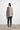 A woman standing against a white wall, wearing a 2 tone gray long-sleeve sweater with asymmetrical hem and black leggings.