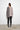 A woman standing against a white wall, wearing a 2 tone gray long-sleeve sweater with asymmetrical hem and black leggings.