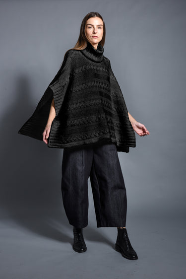 Woman modeling a black knit poncho, wide-leg pants and boots against gray backdrop, Simply Mila modern women's clothing