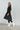 Woman wearing a black dress and white boots against a plain background