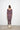 Person wearing a purple dress with scoop neckline standing against a white wall.