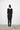 Person wearing a black dress with scoop neck standing against a white wall.
