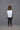 A woman modeling a 2 tone white and black boxy shirt with dolman sleeves, paired with black leggings and strappy sandals, standing against a textured wall.