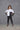 A woman modeling a 2 tone white and black boxy shirt with dolman sleeves, paired with black leggings and strappy sandals, standing against a textured wall.