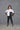 A woman modeling a 2 tone white and black boxy shirt with dolman sleeves, paired with black leggings and strappy sandals, standing against a textured wall.