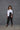 A woman modeling a 2 tone white and black boxy shirt with dolman sleeves, paired with black leggings and strappy sandals, standing against a textured wall.