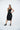 Woman wearing a black sleeveless dress with a leather patch on a white background