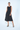 Woman wearing a black sleeveless dress with oversized pockets on a white background