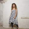 A female model wearing a spaghetti straps polka dots peplum dress with pockets, low neck line, asymmetrical hem, paired with Black leggings, black sandals against an industrial white background.