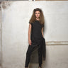 A woman standing in front of a white textured wall wearing a black mesh dress with short sleeves, a round neckline, and a maxi length. She is also wearing black high heels.