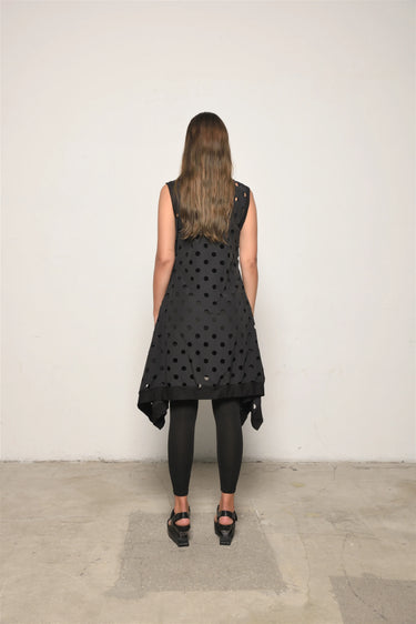 Person wearing a black polka dot dress with a plain white background