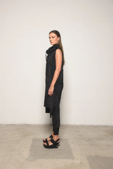 Woman wearing a black sleeveless top and pants against a white wall.