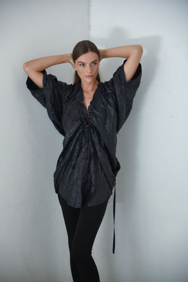 Woman wearing a black oversized shirt and black pants against a white wall