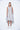 A female model wearing a sleeveless knee-length dress with horizontal black stripes and round neckline, standing against a white background.