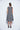 A female model wearing a linen gray sleeveless knee-length dress with vertical stripes and round neckline, standing against a white background.