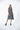 A female model wearing a  linen gray sleeveless knee-length dress with vertical stripes and round neckline, standing against a white background.