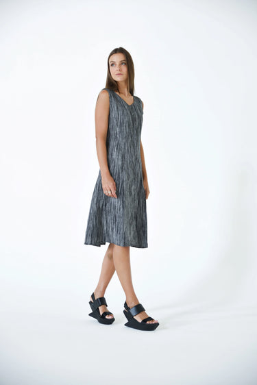A female model wearing a  linen gray sleeveless knee-length dress with vertical stripes and round neckline, standing against a white background.