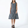 A female model wearing a  linen gray sleeveless knee-length dress with vertical stripes and round neckline, standing against a white background.