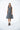 A female model wearing a  linen gray sleeveless knee-length dress with vertical stripes and round neckline, standing against a white background.