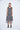 A female model wearing a linen gray sleeveless knee-length dress with vertical stripes and round neckline, standing against a white background.