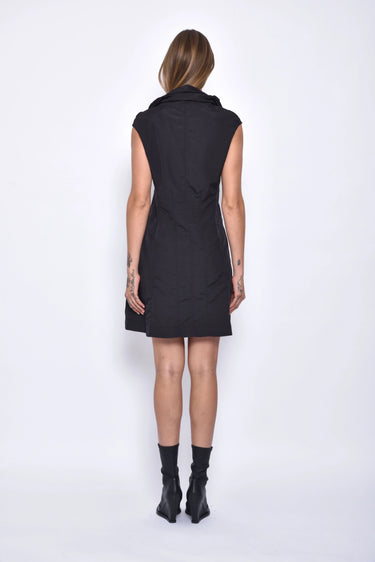 A woman wearing a black sleeveless mini dress with a high collar, pockets and front zipper.