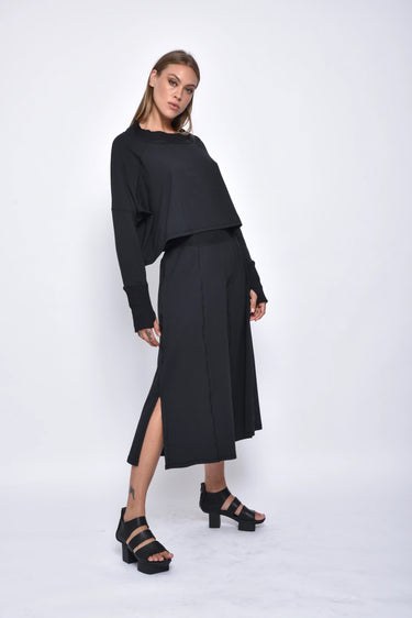 A female model wearing a black long sleeve top and black cropped pants, with white background