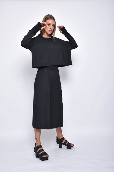 A female model wearing a black long sleeve top and black cropped pants, with white background