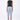 A female model wearing a Black sleeveless top with black abstract paint design on the sides and a long light blue pants over a white background.