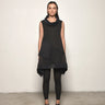 A woman modeling a sleeveless black tunic with a draped cowl neck and Asymmetrical hem, paired with black leggings.