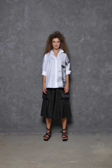 A model wearing a white boxy shirt with black strokes and black culotte pants.