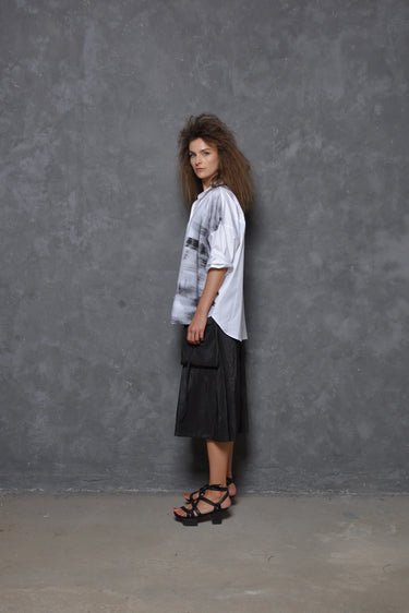 A model wearing a white boxy shirt with black strokes and black culotte pants.