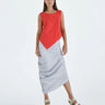 A female model wearing a Red sleeveless top, uneven hem, Black horizontal striped asymmetrical skirt and sandals against a white background