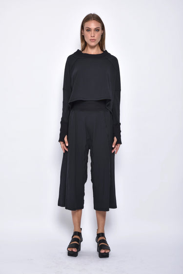 A female model wearing a black long sleeve top and black cropped pants, with white background