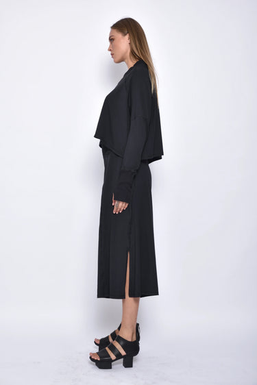 A female model wearing a black long sleeve top and black cropped pants, with white background