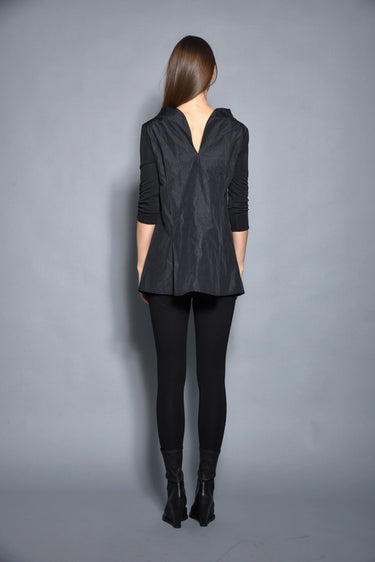 A woman modeling a black top with 3/4 sleeves and textured pattern, paired with black leggings and black boots against a gray background