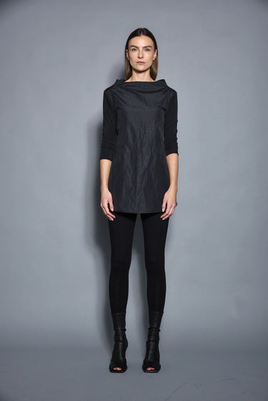 A woman modeling a black top with 3/4 sleeves and textured pattern, paired with black leggings and black boots against a gray background