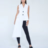 A model wearing an asymmetrical white vest with no sleeves, paired with black pants and black sandals.