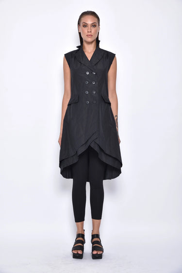 A woman wearing a sleeveless black trench-style Vest with a double-breasted button front, notched lapel collar and flap pockets on either side of the waist, asymmetrical hem line, paired with black leggings and chunky black open-toe heels over a white background.