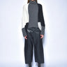 Model wearing a gray turtleneck, black and white cardigan, black pants, and black boots on a light blue background