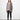 A woman standing against a white wall, wearing a 2 tone gray long-sleeve sweater with asymmetrical hem and black leggings.