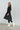 Woman wearing a black dress and white boots against a plain background