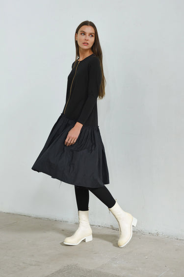 Woman wearing a black dress and white boots against a plain background