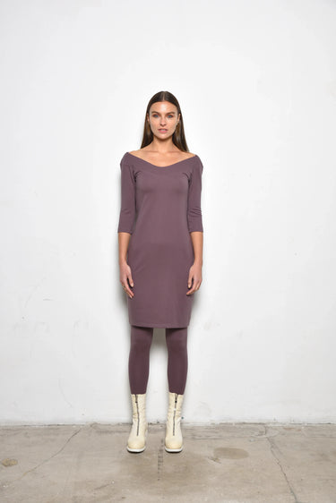 Woman wearing a purple dress with scoop neckline and white boots against a plain white background