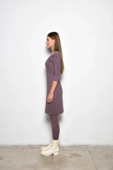 Woman wearing a purple dress and white boots against a white wall