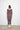 Person wearing a purple dress with scoop neckline standing against a white wall.