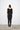 Person wearing a black dress with scoop neck standing against a white wall.