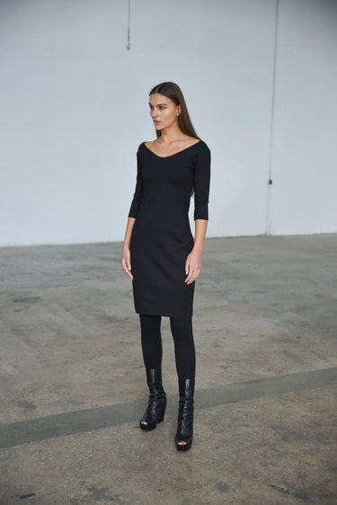 Woman wearing a black dress with scoop neck and black boots in an industrial setting