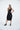 Woman wearing a black sleeveless dress with a leather patch on a white background